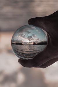 Close-up of hand holding crystal ball against sky