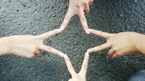 Directly above shot of cropped friends joining fingers on road