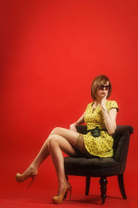 Woman sitting on chair against red background