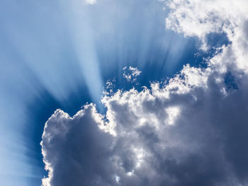 Low angle view of sunlight streaming through clouds