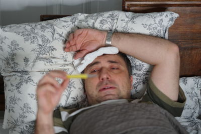 Man checking temperature while lying on bed at home