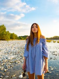 Portrait of beautiful young woman standing by lake against sky