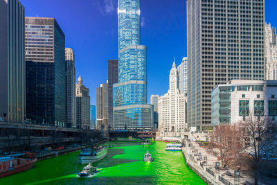 Modern buildings by canal in city against sky