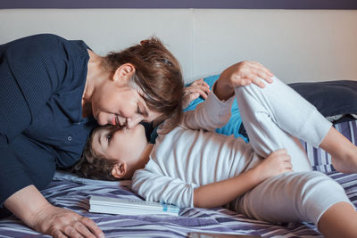 Grandson kissing grandmother while on bed at home