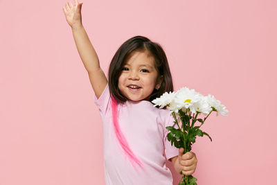 Portrait of young woman holding flowers against pink background