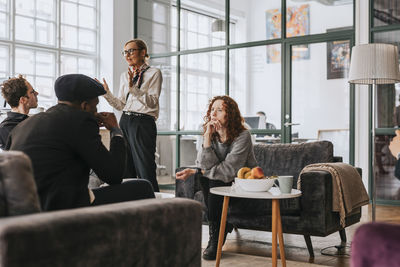 Businesswoman with hand on chin discussing with colleague sitting on sofa at office