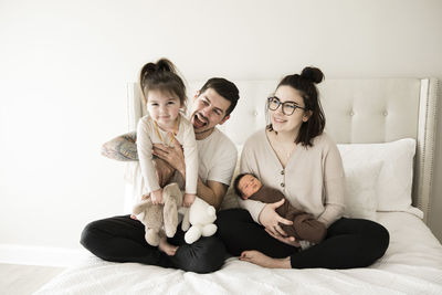 Modern millennial family with toddler and newborn plays on white bed