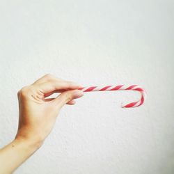 Cropped hand holding candy cane against white wall at home