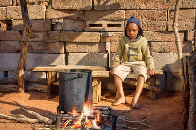Portrait of boy sitting by campfire in village