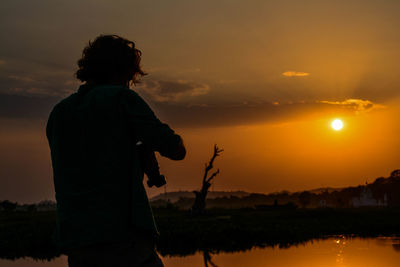 Silhouette man standing at lakeshore against sky during sunset