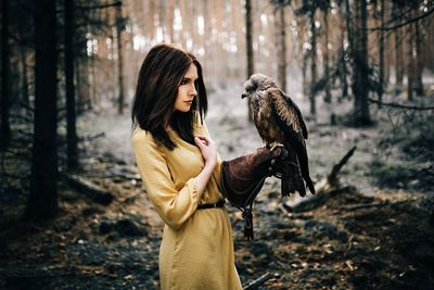 Beautiful woman standing with hawk in forest