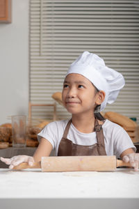 A child wearing a white chef hat, brown apron and smiling with happiness.