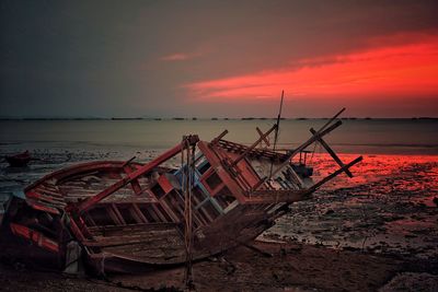 Abandoned boat moored on beach against sky during sunset