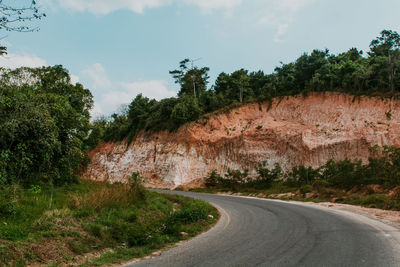 Road by trees and hill against sky