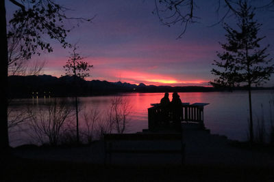 Silhouette plants by lake against sky during sunset
