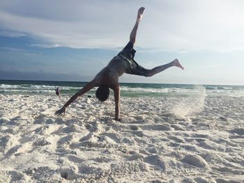 Full length of man doing cartwheel at beach against sky