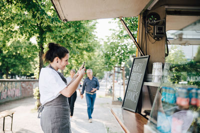 Female owner photographing board through smart phone while standing by food truck