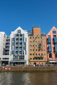 Buildings by river against clear blue sky