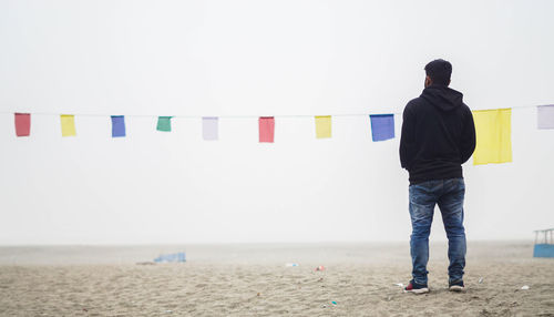 Rear view of man standing on beach against clear sky