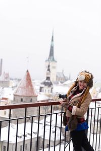 Woman holding camera while standing by railing at observation point during winter