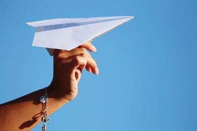 Cropped hand of woman holding paper airplane against clear blue sky