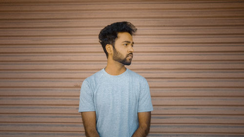 Young man looking away while standing against wall