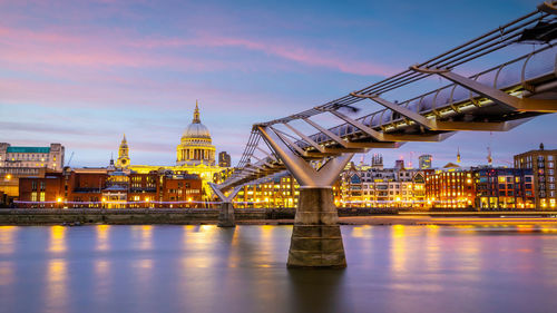 Illuminated bridge over river against sky at sunset