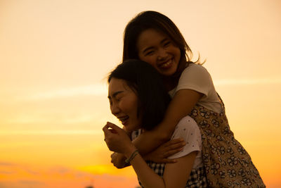 Woman piggybacking friend against sky during sunset