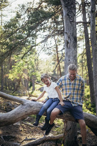 Full length of man sitting on tree trunk in forest