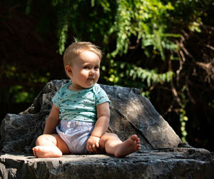 Cute boy looking away while sitting on rock