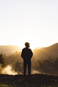 Rear view of man standing on field against sky during sunset