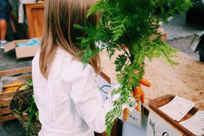 Rear view of girl selling fresh carrots at farmer market