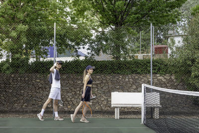 Side view of man and woman dressed in sports arriving at tennis court to play a match with racquets