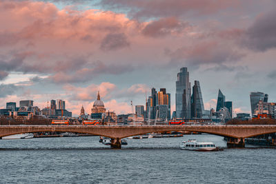 Bridge over river by buildings against sky in city