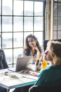 Young businesswoman looking away while sitting at conference table during meeting in office