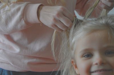 Portrait of girl smiling against mother styling her hair at home