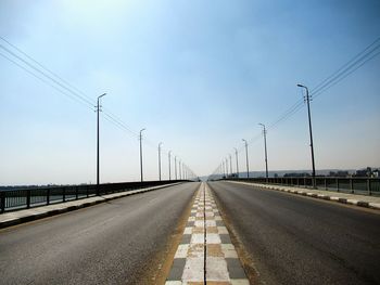 Road by electricity pylon against sky