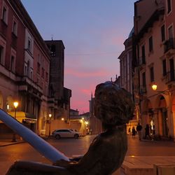 Illuminated street amidst buildings against sky at sunset