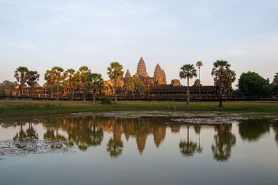 Reflection of trees in lake by building against sky at angkor wat temple, cambodia