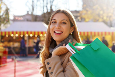 Portrait of smiling young woman looking at camera carrying shopping bags at the christmas markets