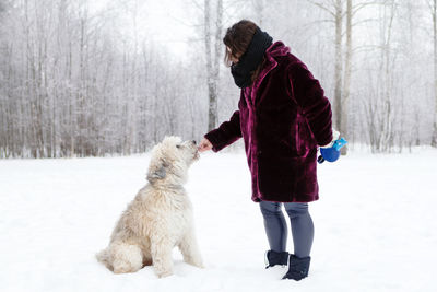 Full length of woman with dog on snow covered field