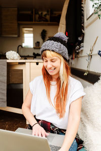 Delighted female traveler sitting outside on stairs of van while working remotely on laptop looking away