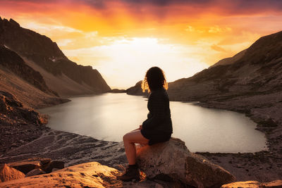 Man sitting on rocks at shore against sky during sunset