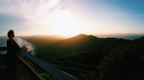 Woman looking at landscape against sky during sunset