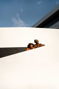 From below cheerful stylish african american man and woman embracing while standing on modern street stairs looking away in sunset light