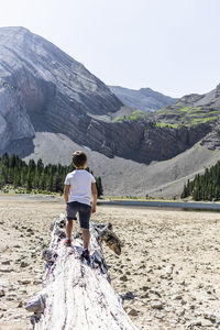 Rear view of boy walking on wood against mountain