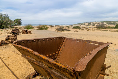 Close-up of abandoned rusty vehicle part on field against sky