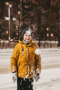 A boy in a yellow jacket plays with snow during a snowfall