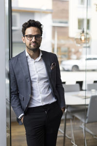 Portrait of confident male real estate agent standing with hands in pockets at office