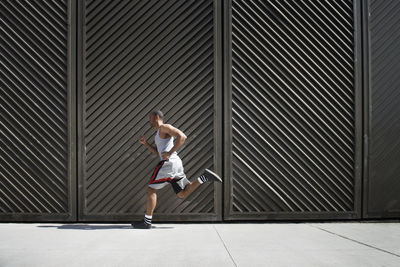 Side view of man running on floor against metal wall